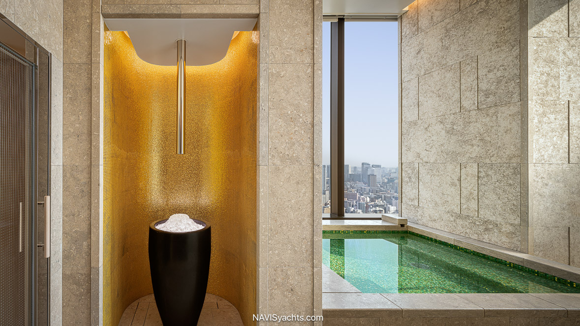 An impeccably designed suite at the Bvlgari Hotel Tokyo, featuring warm wood-lined walls, a bed adorned with exquisite Hosoo textiles facing a panoramic city view, and custom dark oak furniture.