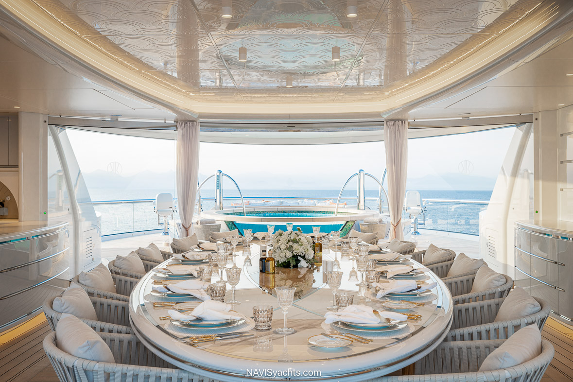 Elegant alfresco dining area aboard Kismet featuring a grand table set for 14, overlooking a Jacuzzi and panoramic ocean views.