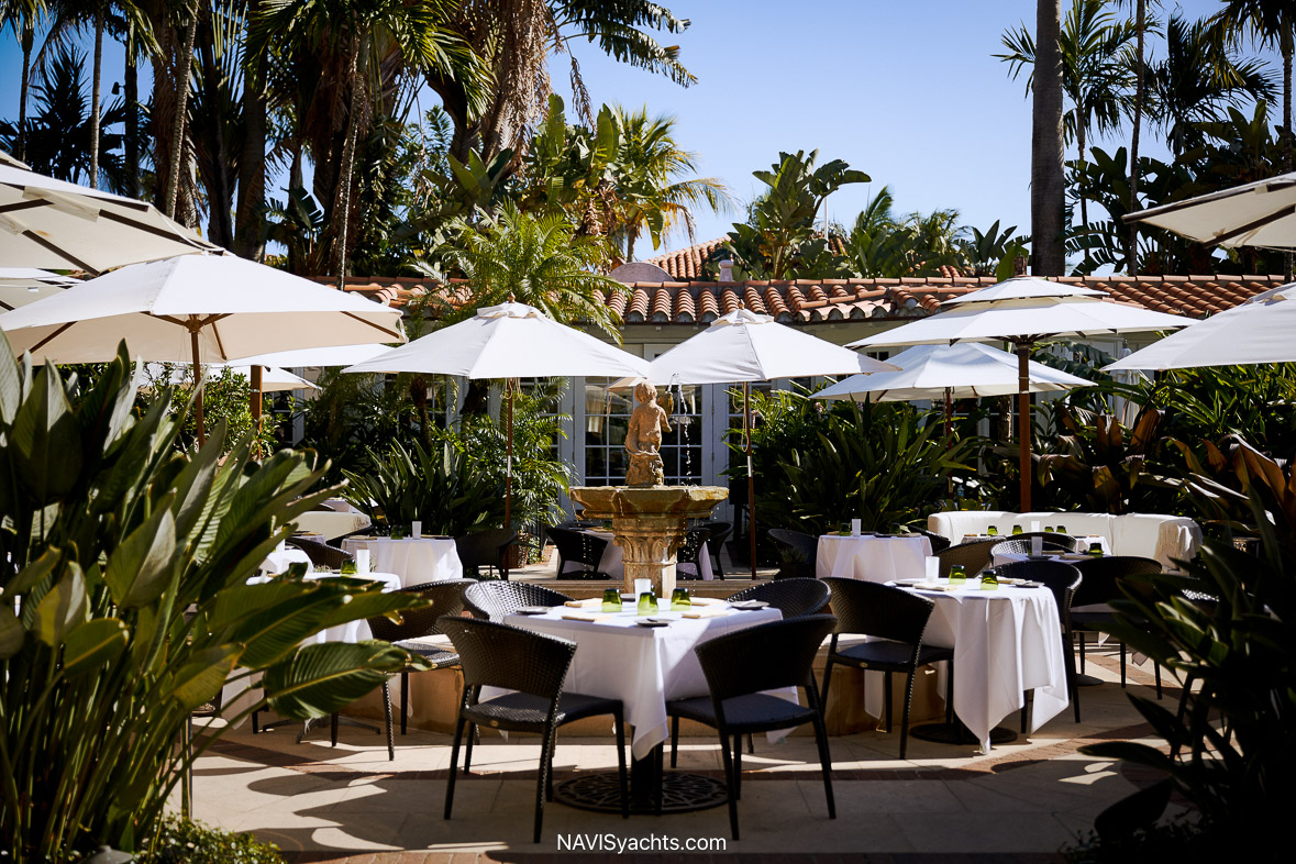 Elegant outdoor setting of Café Boulud in Palm Beach with fine dining table setup, surrounded by lush greenery and a serene fountain.